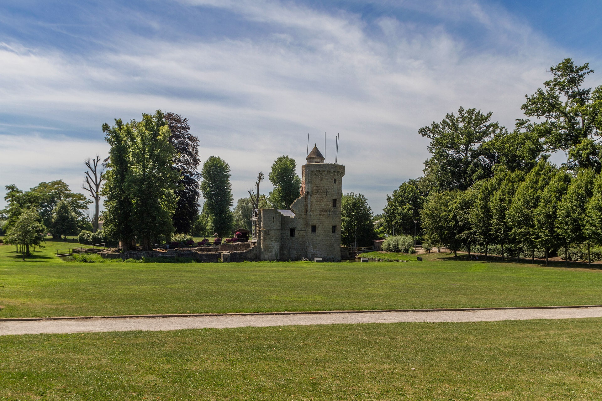 Historische burcht van Herzele met stenen toren omringd door groene bomen en grasveld onder bewolkte hemel