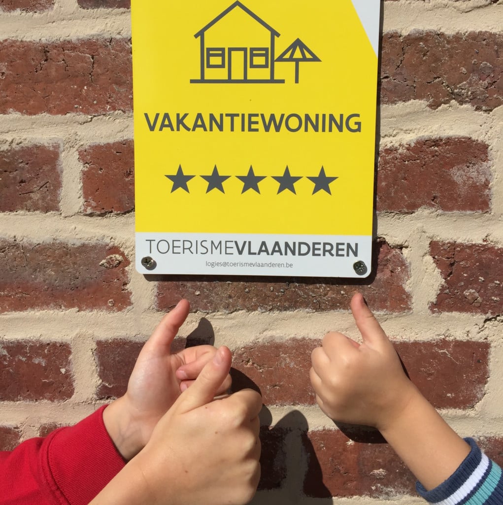 Twee handen tonen duimen omhoog voor gele vakantiewoning classificatie plaat met 5 sterren van Toerisme Vlaanderen