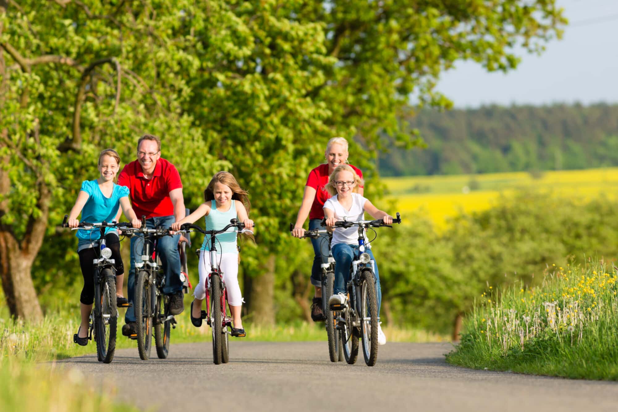 Familie van vijf personen fietst samen op landelijke weg door groene Vlaamse Ardennen landschap
