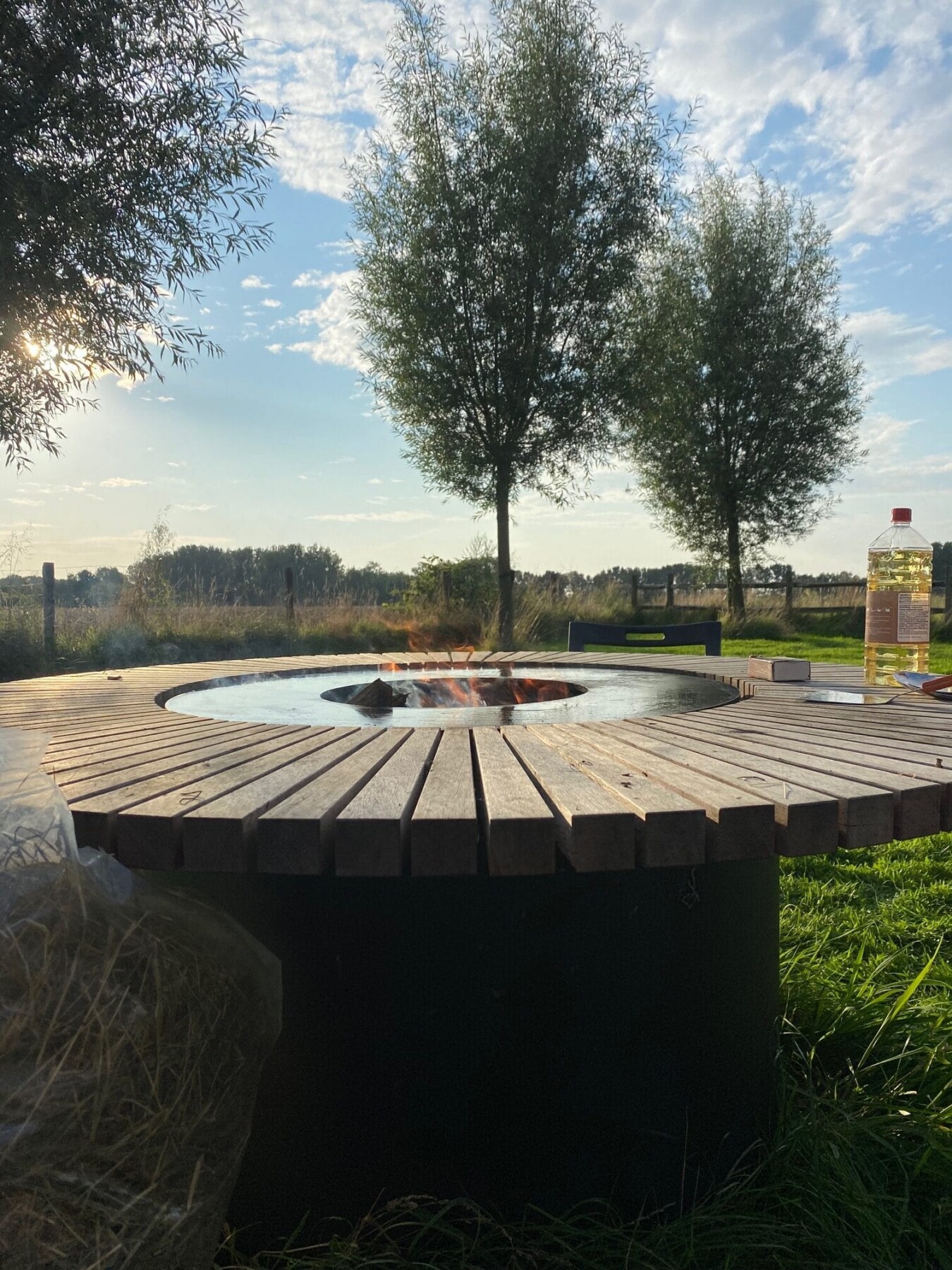 Ronde houten teppanyakitafel met centrale vuurplaats in landelijke tuin met bomen en heuvels op de achtergrond