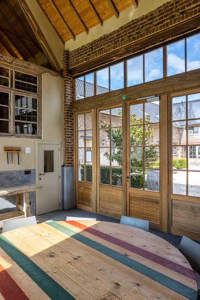 Moderne vergaderruimte met houten tafel, bakstenen muren en glazen deuren in Eyndevelde vakantiewoning