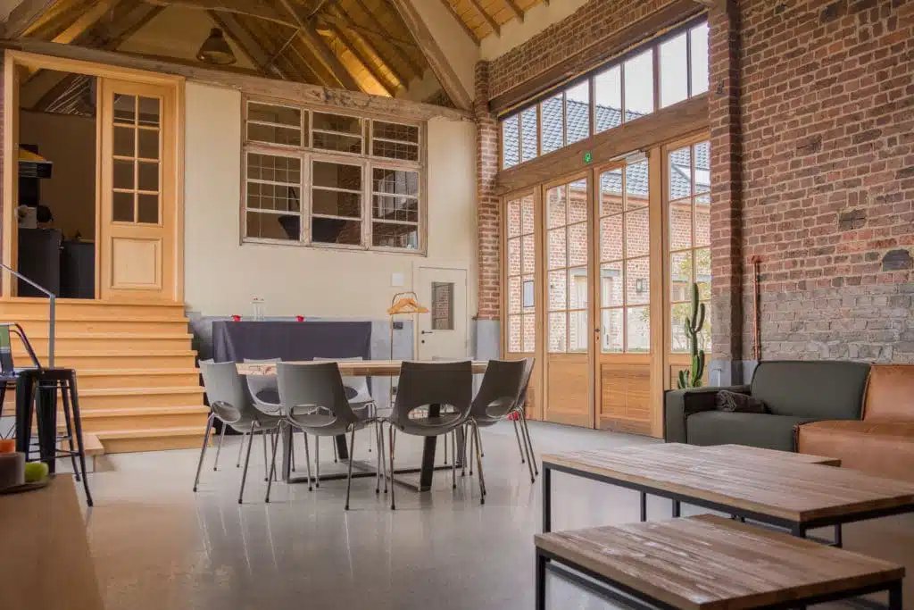 Modern vergaderzaal in gerenoveerde hoeve met exposed brick muren, houten balken en glazen deuren naar binnenplaats