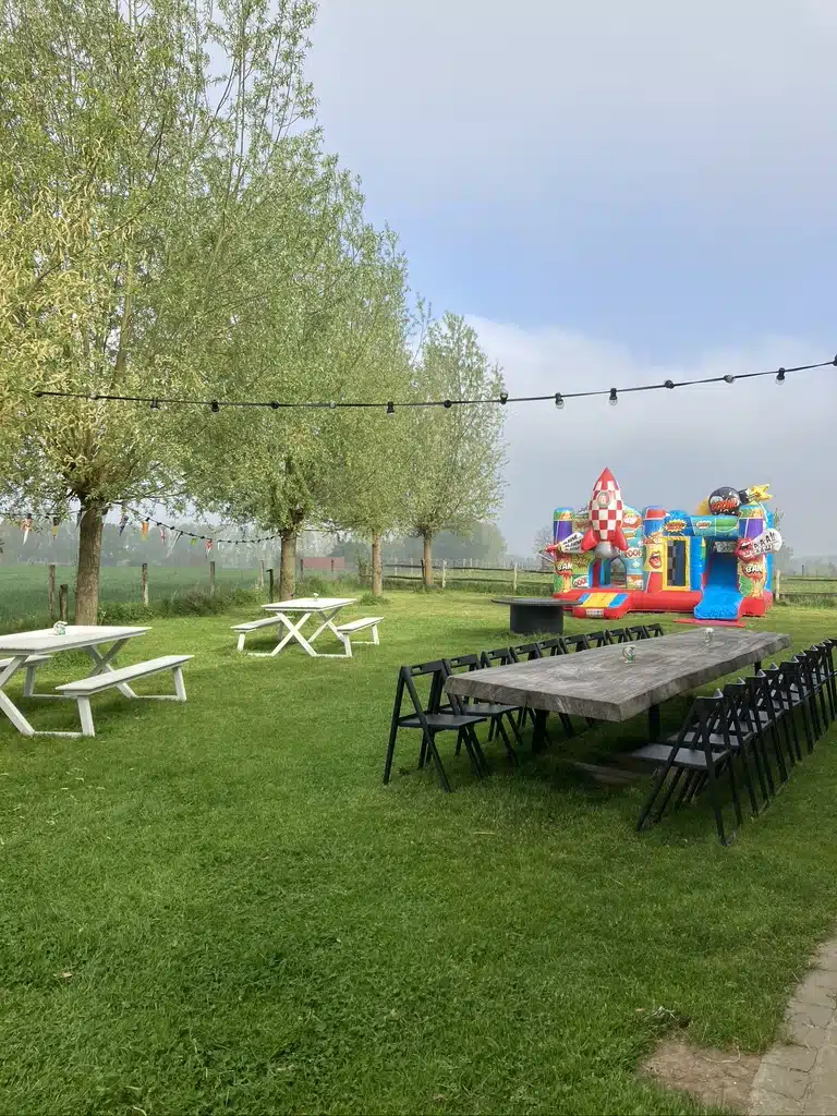 Outdoor feestopstelling met picknickbanken, lange tafel en kleurrijke springkasteel in groene tuin van Eyndevelde