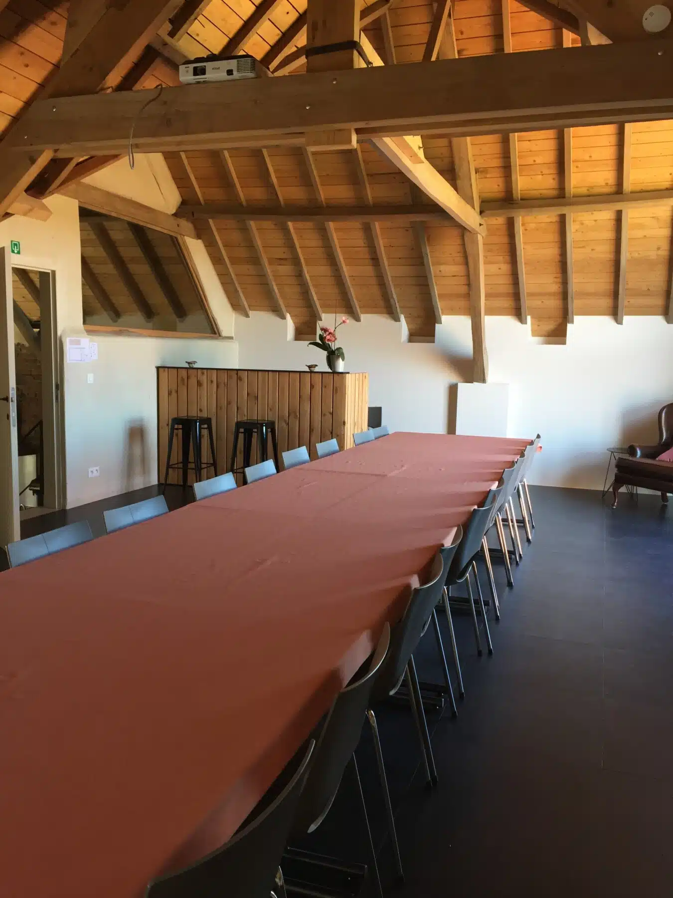 Ruime vergaderzaal met lange tafel en stoelen onder houten balkenplafond in Eyndevelde vakantiewoning