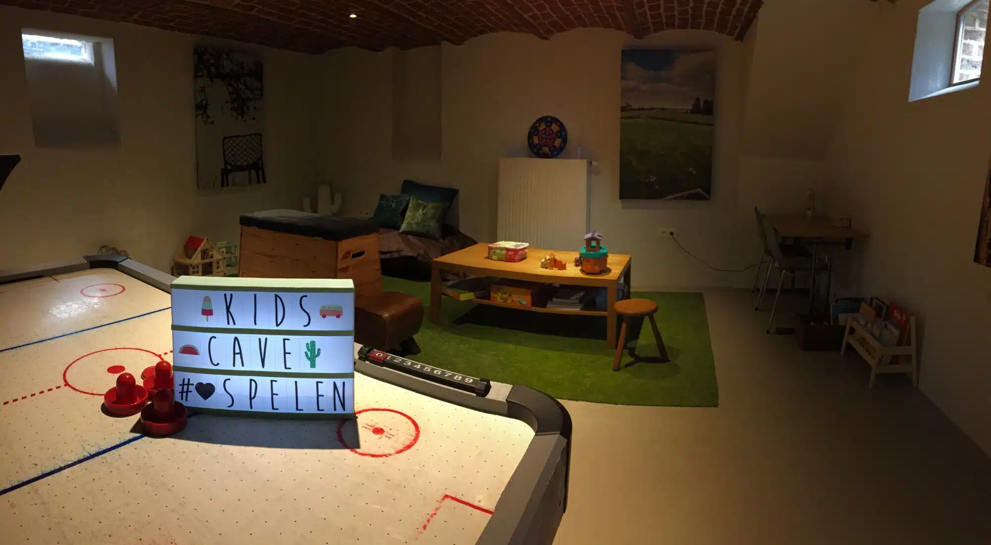 Kinderspeelkamer met air hockey tafel, lightbox "KIDS CAVE SPELEN", groene speelmat en houten meubels