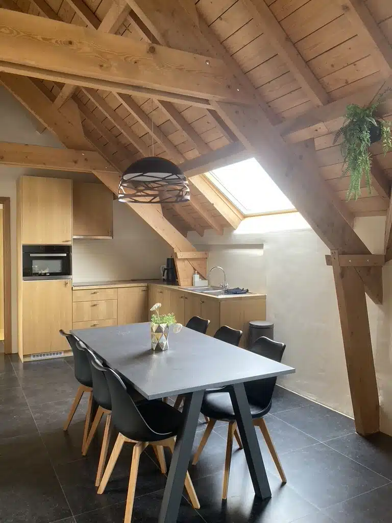Gezellige zolderkeuken met houten dakbalken, eettafel met zwarte stoelen, inbouwkeuken en daklicht bij Eyndevelde