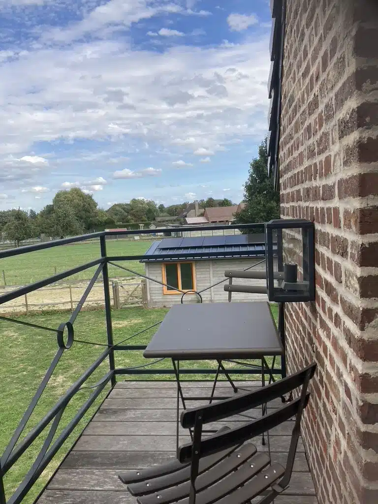 Balkon van Eyndevelde met zwarte bistrotafel en stoelen, uitzicht op groene weide, houten schuur met zonnepanelen en landelij