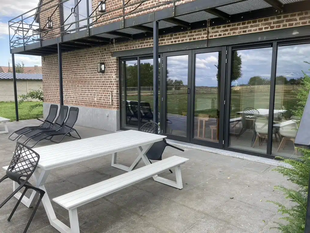 Buitenterras van Eyndevelde met witte picknicktafel, zwarte ligstoelen en grote glazen schuifdeuren aan een moderne bakstenen