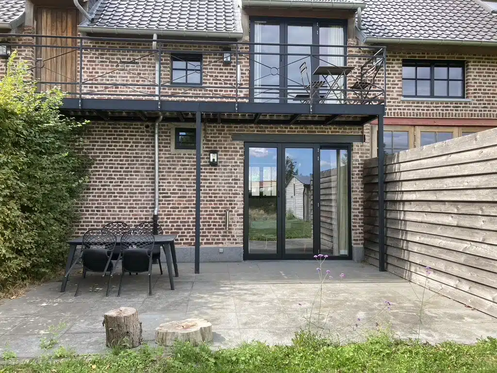 Terras van vakantiewoning Eyndevelde met zwarte tuinset, overdekt balkon en glazen schuifdeuren in rustieke bakstenen gevel