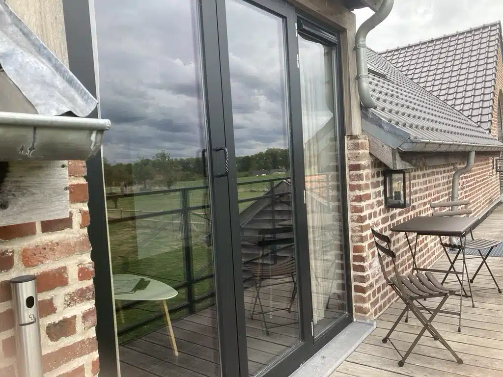 Terras van Eyndevelde met grijze schuifdeuren, bakstenen muren, houten vloer, bistrostoelen en uitzicht op groen landschap on