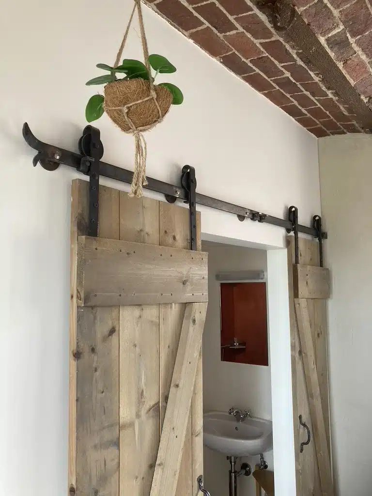 Rustieke schuifdeuren van hout met zwart metalen rail in badkamer van Eyndevelde, met hangplant in kokosbol en bakstenen plaf