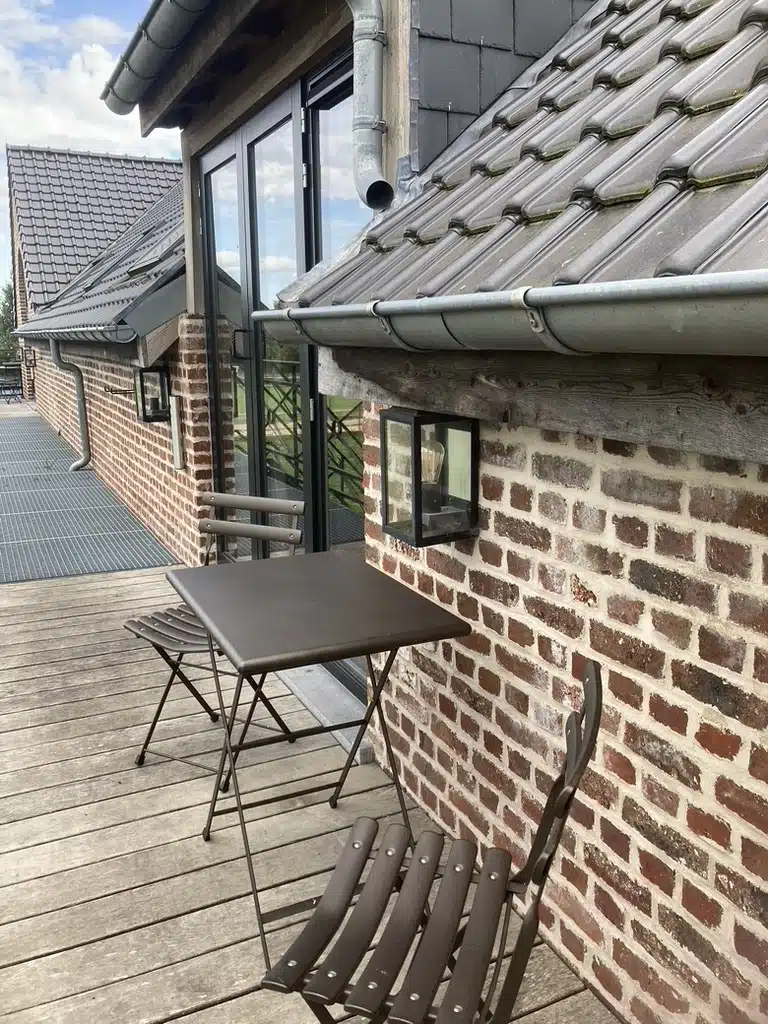 Gezellig terras met bistrotafel en stoelen op houten vlonder bij bakstenen muur met lantaarn, Eyndevelde vakantieverblijf